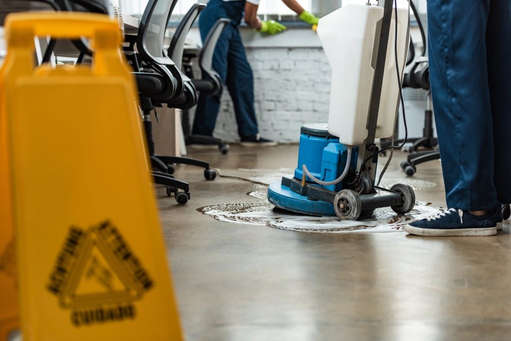 cropped view of cleaner washing floor with cleaning machine near colleague