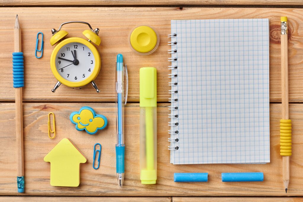 Alarm clock and school stationary on wooden background.
